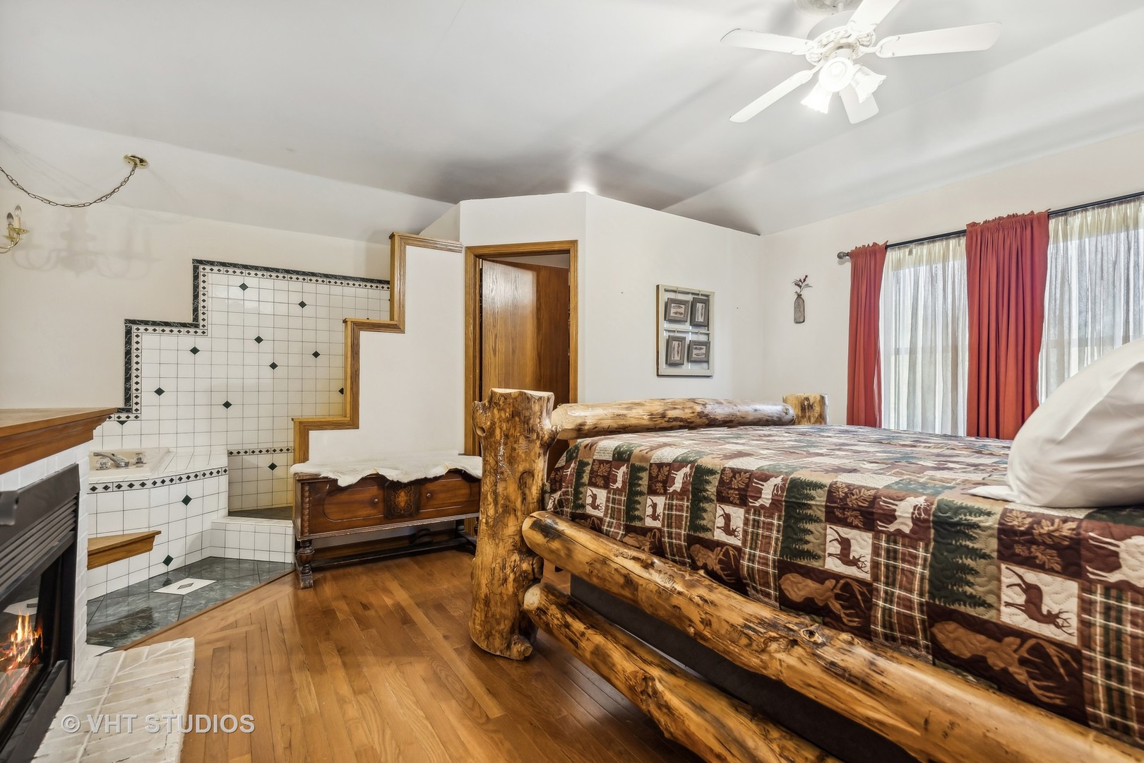 Bedroom with a rustic log bed, patterned quilt, and sunken tiled tub area.