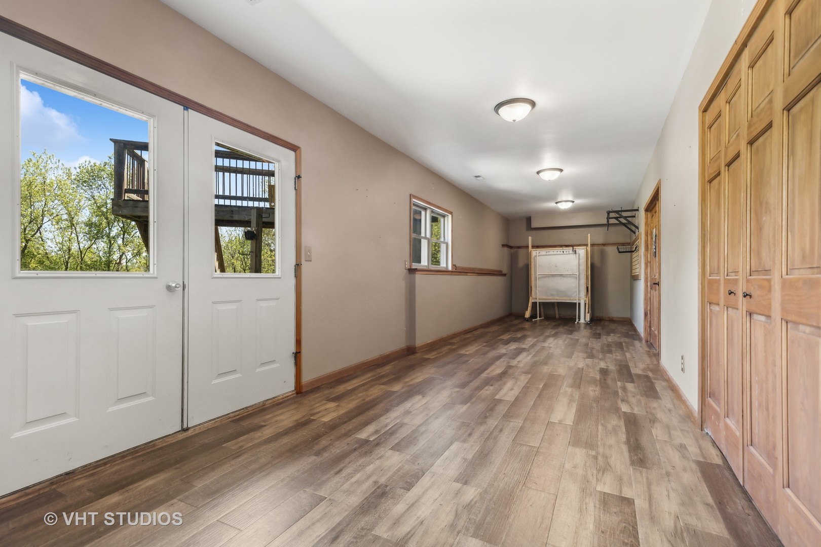 Long finished room with wood-look flooring, tall wooden cabinets, and windowed exterior doors.