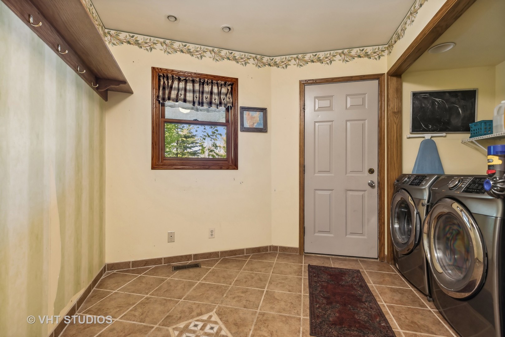 Laundry room with front-loading washer and dryer, tiled floor, window, and exterior door.