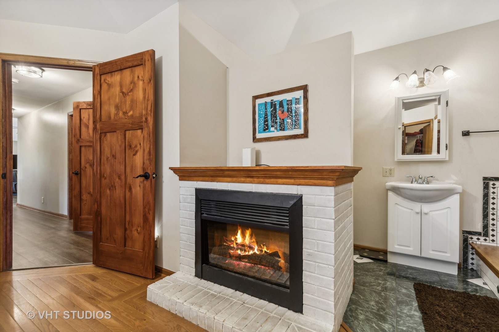Bathroom with a lit white-brick fireplace, white vanity sink, and rustic wooden doors.