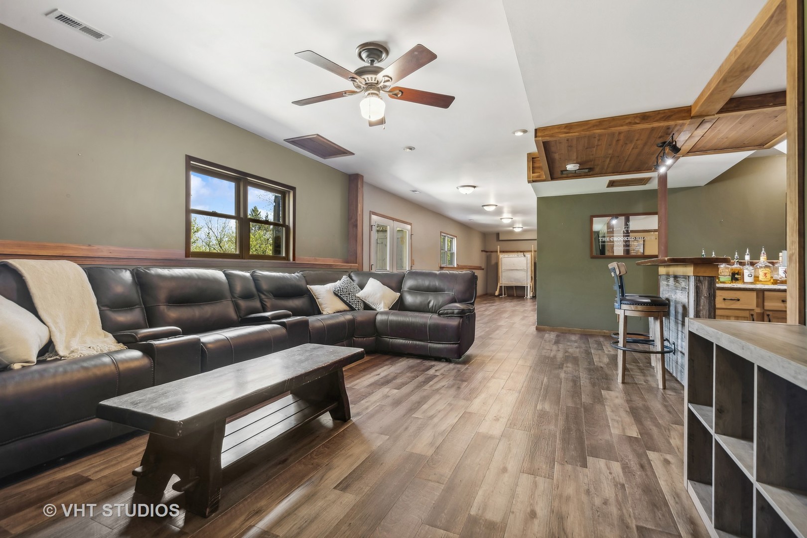 Furnished lounge with a leather sectional, wood-plank flooring, and a rustic bar.