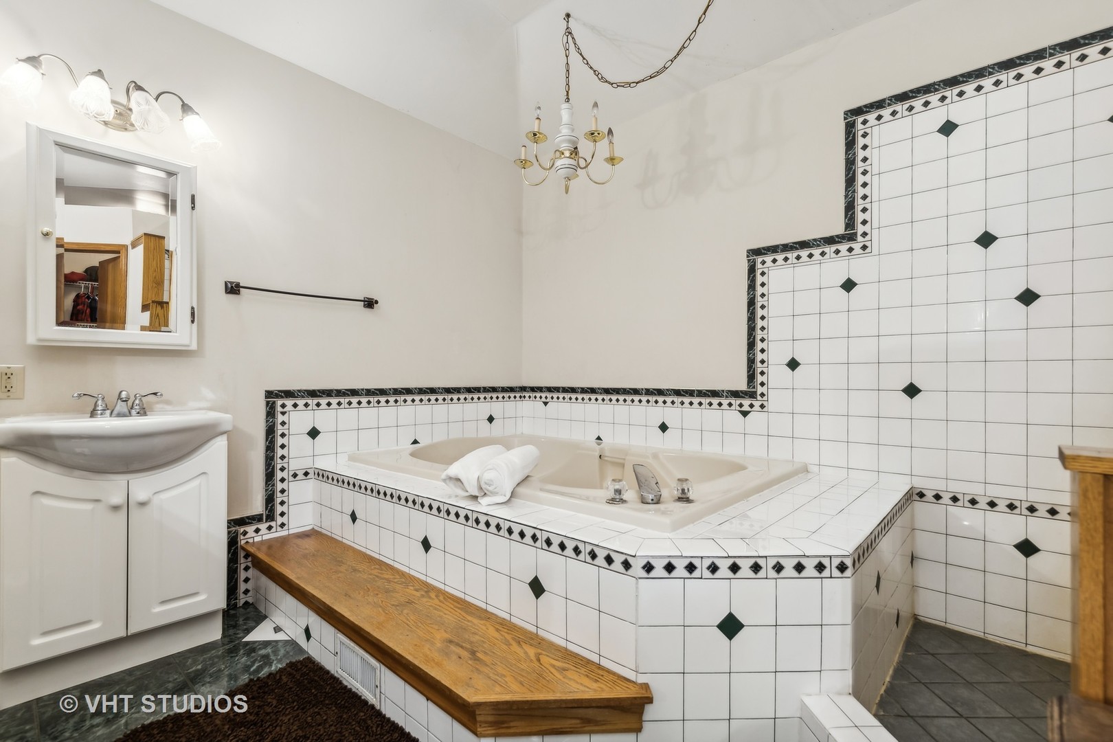 Bathroom with a tiled corner whirlpool tub, white vanity, and long wooden bench.