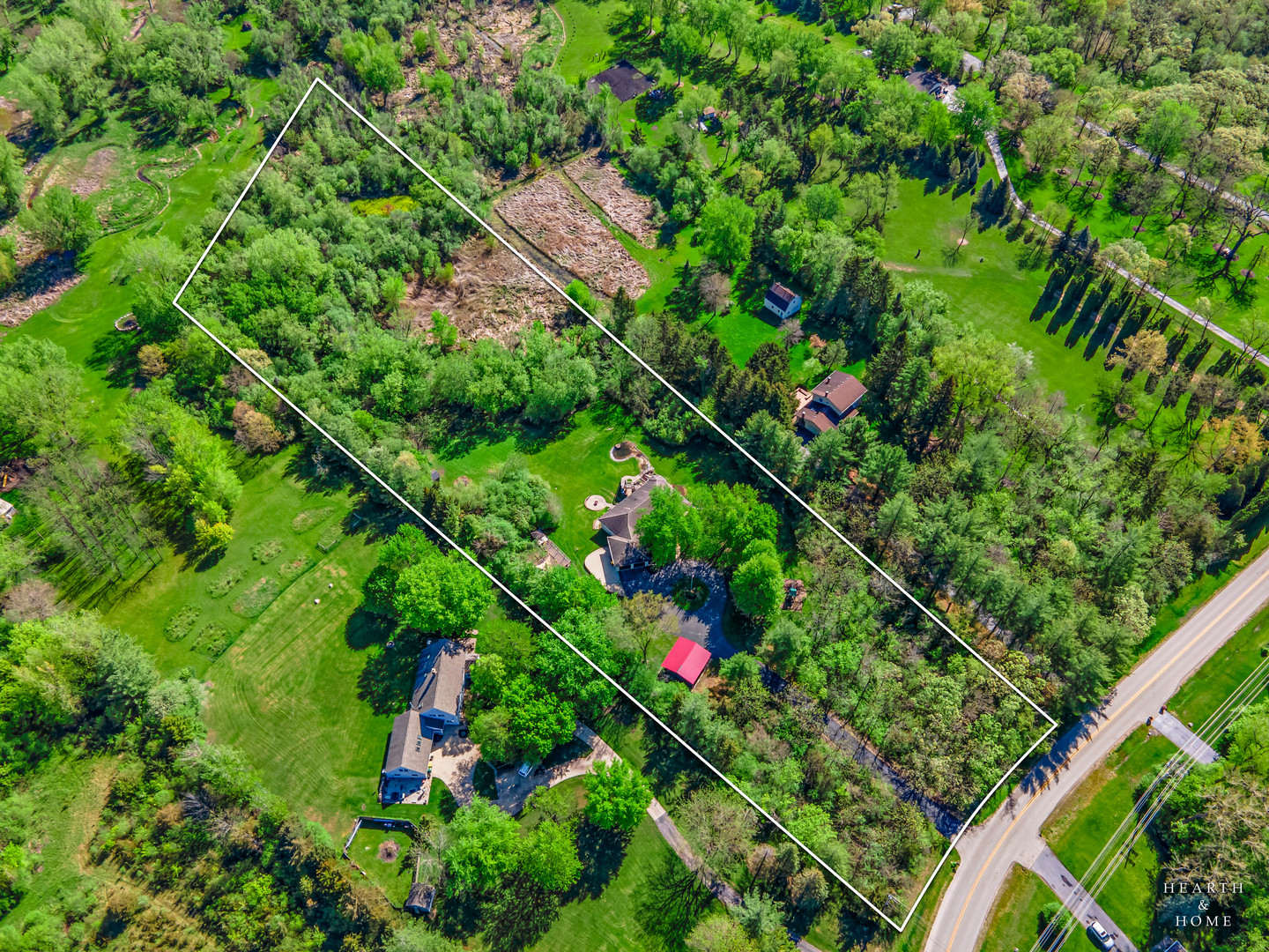 Aerial view of a wooded property outlined in white, with a house, lawn, and road frontage.