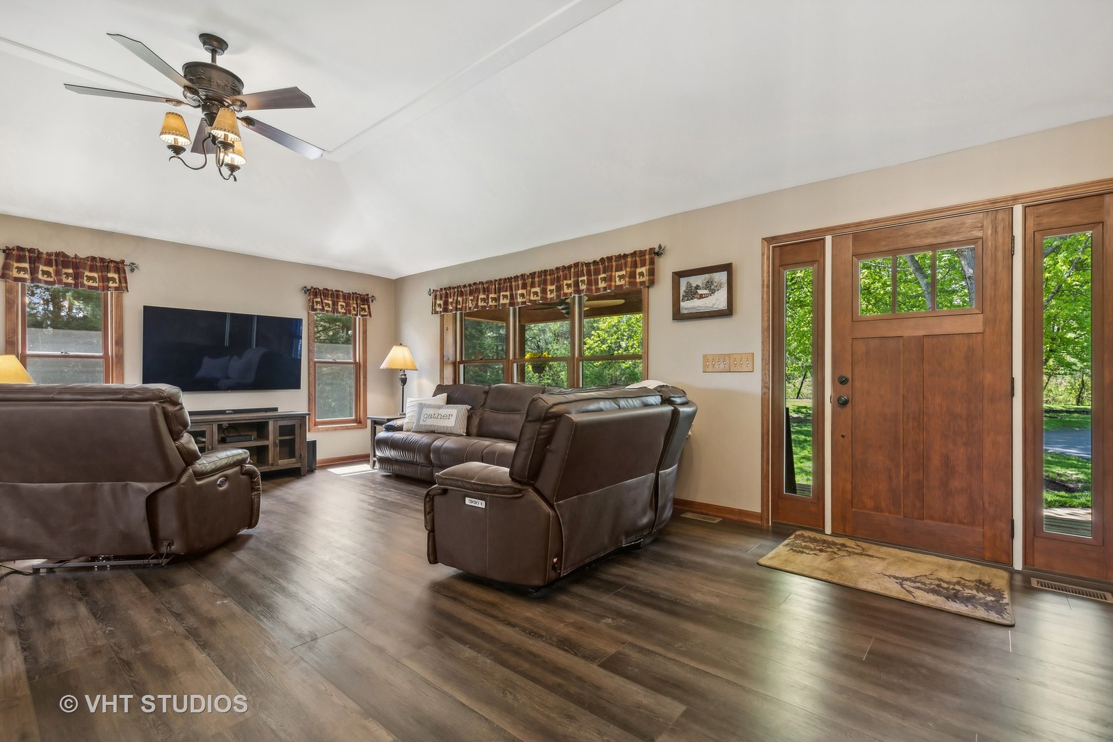 Living room with brown leather recliners, dark flooring, and a wood front door with glass sidelights.