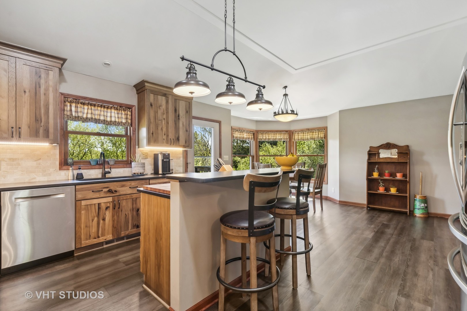 Kitchen with wood cabinetry, a large island with bar stools, and a dining area by bay windows.