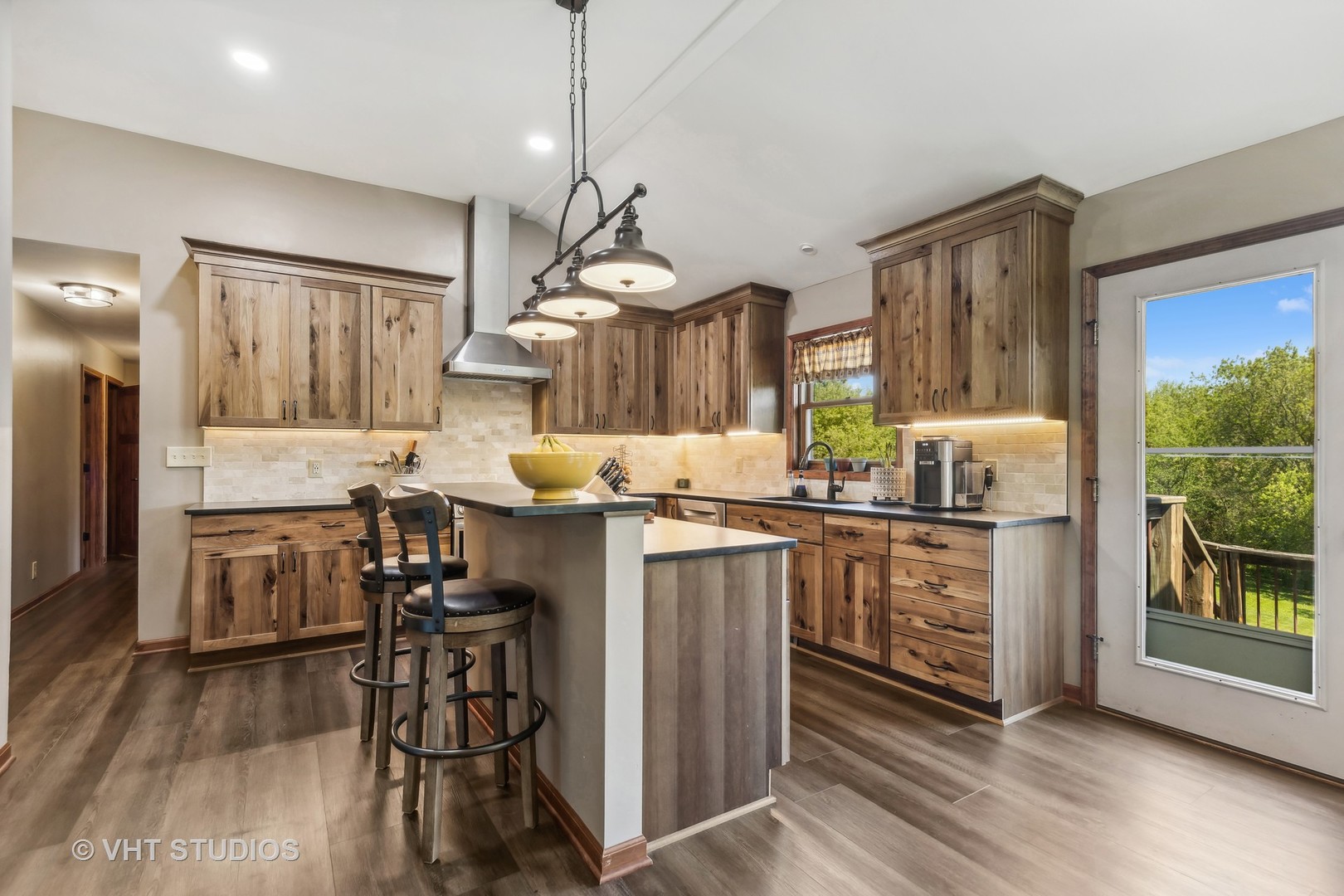 Kitchen with rustic wood cabinetry, a central island, pendant lights, and a glass door to the deck.