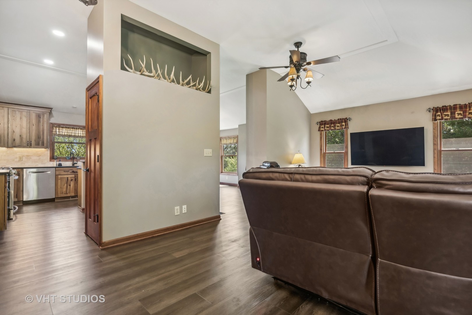 Living room with a leather sectional, ceiling fan, and antlers displayed in a wall niche.