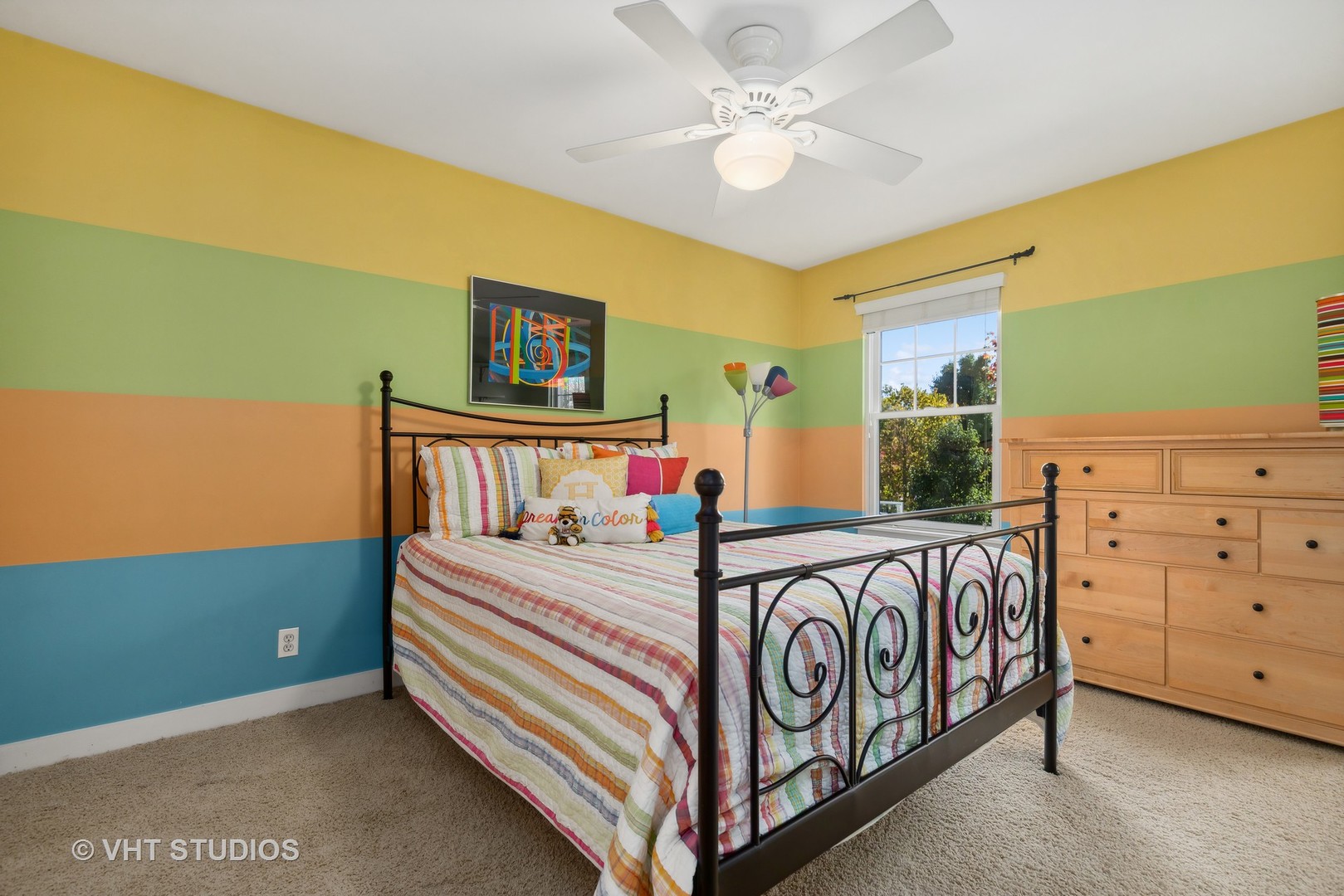 Bedroom with a black metal bed, colorful striped bedding, and bold multicolored walls.