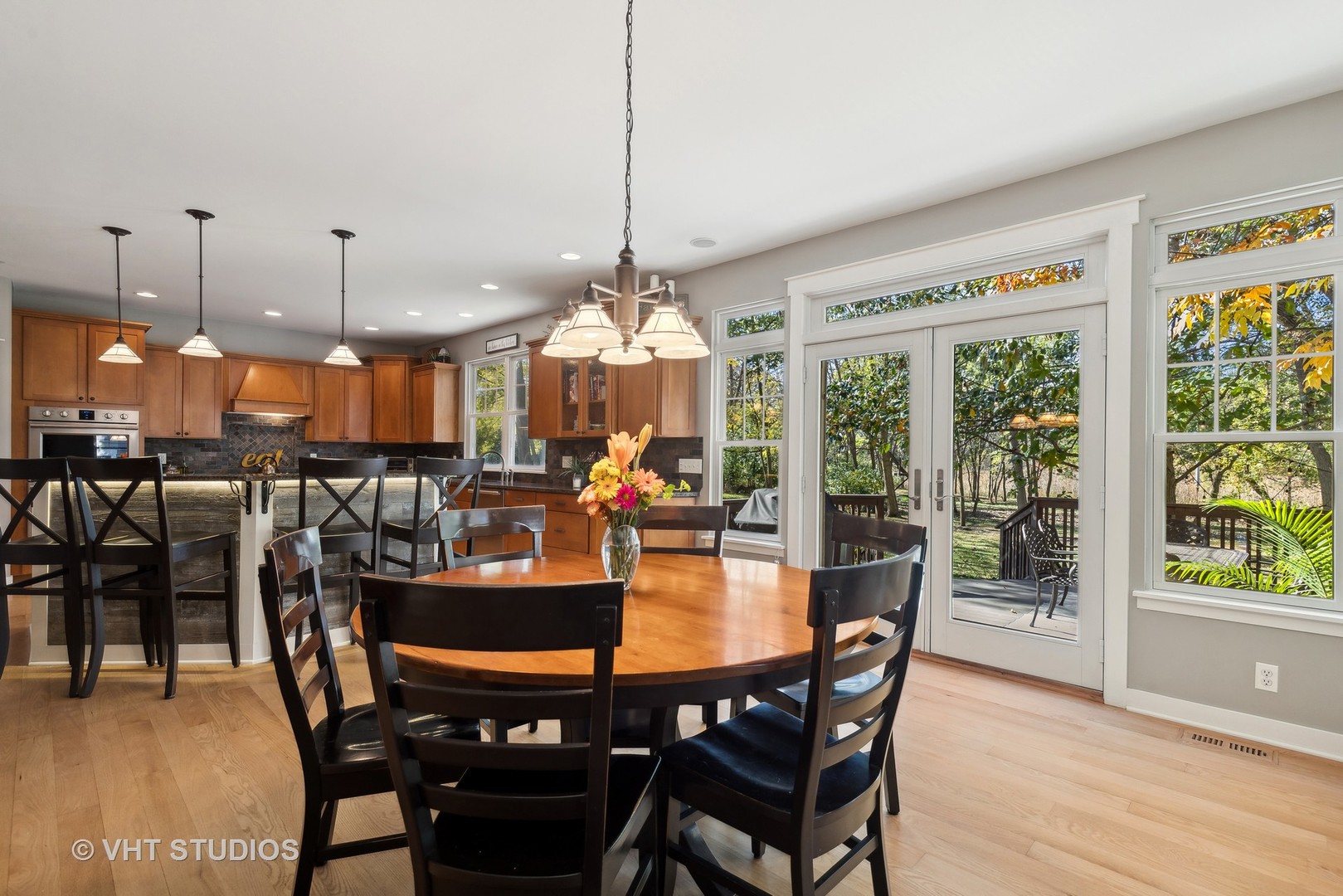 Dining area beside a wood-cabinet kitchen, with glass doors opening to a leafy deck.