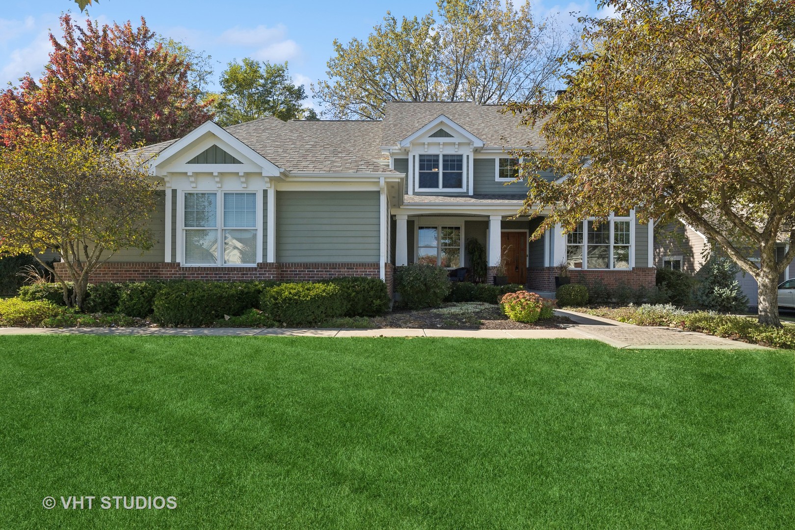 Gray two-story home with brick accents, a covered entry, and autumn trees framing the front lawn.