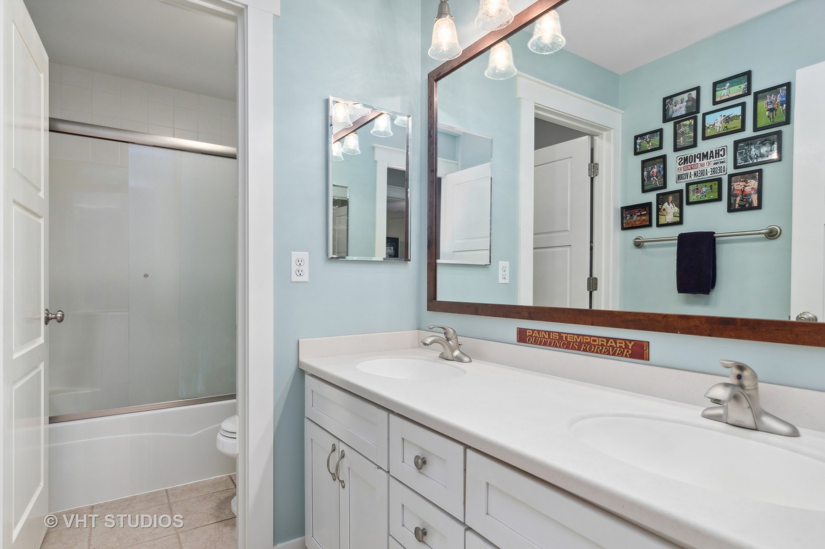 Bathroom with a double-sink vanity, large wood-framed mirror, and glass-enclosed tub and shower.