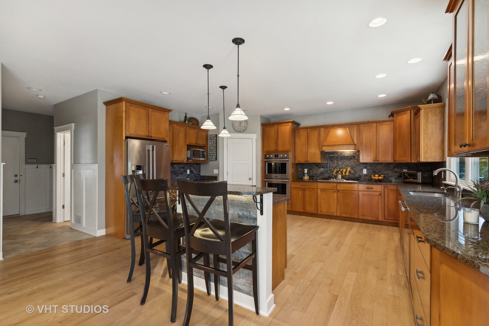 Kitchen with honey-colored cabinets, granite counters, stainless appliances, and an island with bar seating.
