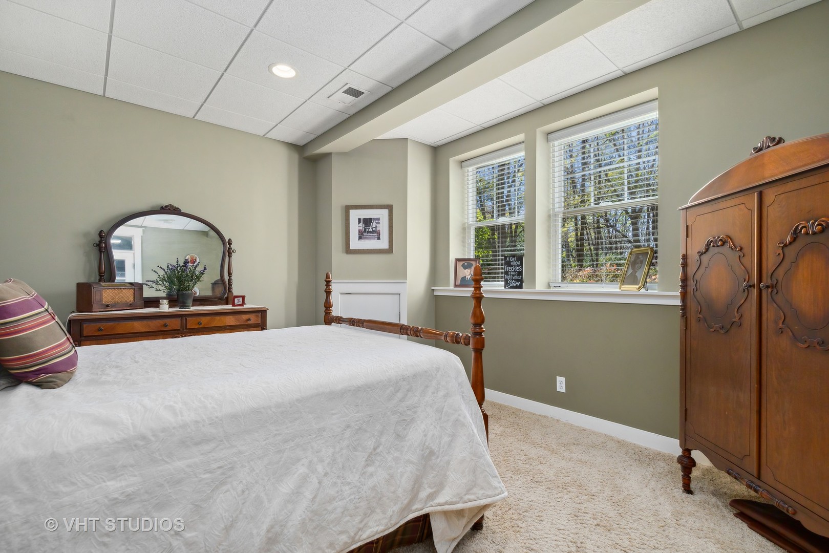 Bedroom with a white-covered bed, ornate dark wood furniture, and two windows overlooking trees.