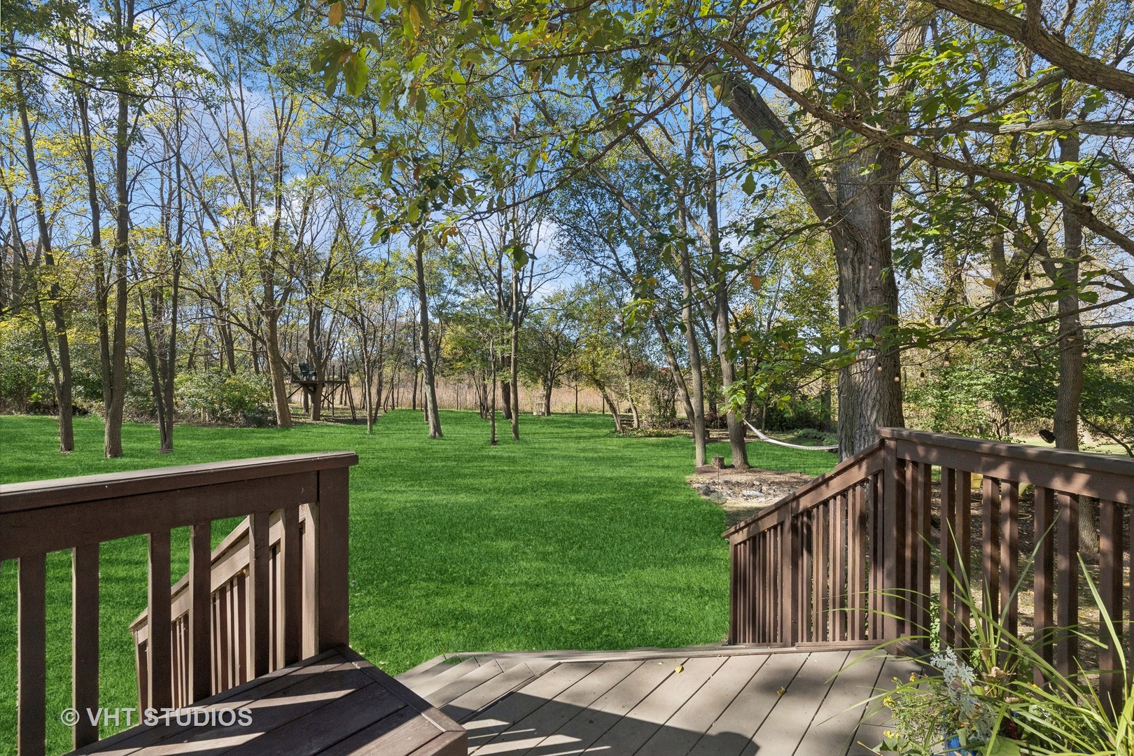 Wooden deck overlooking a tree-filled lawn with a hammock and play structure.