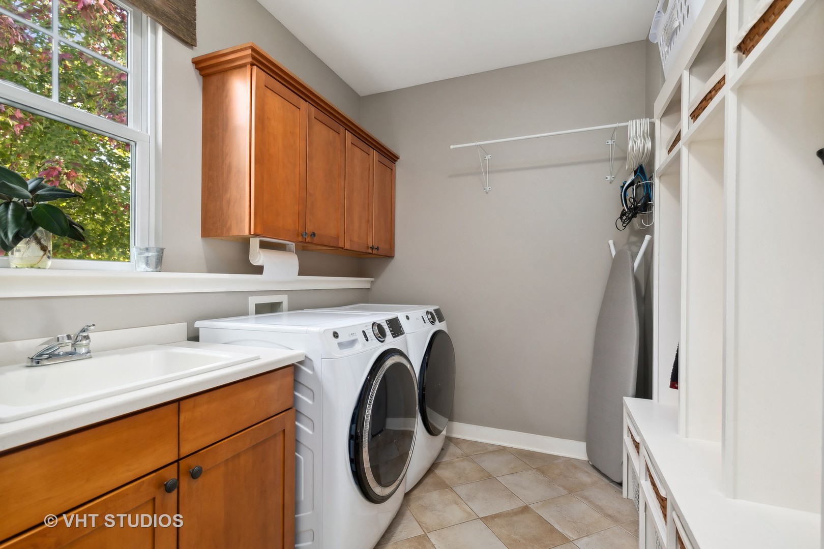 Laundry room with front-loading washer and dryer, utility sink, wood cabinets, and built-in shelving.
