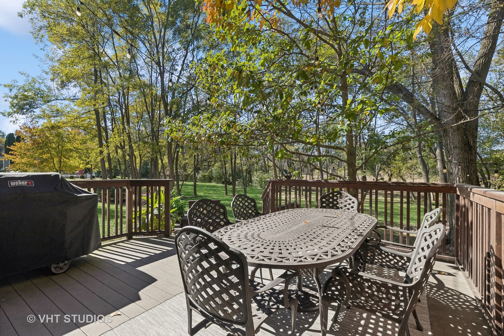 Wooden deck with outdoor dining set and covered grill overlooking a leafy yard.