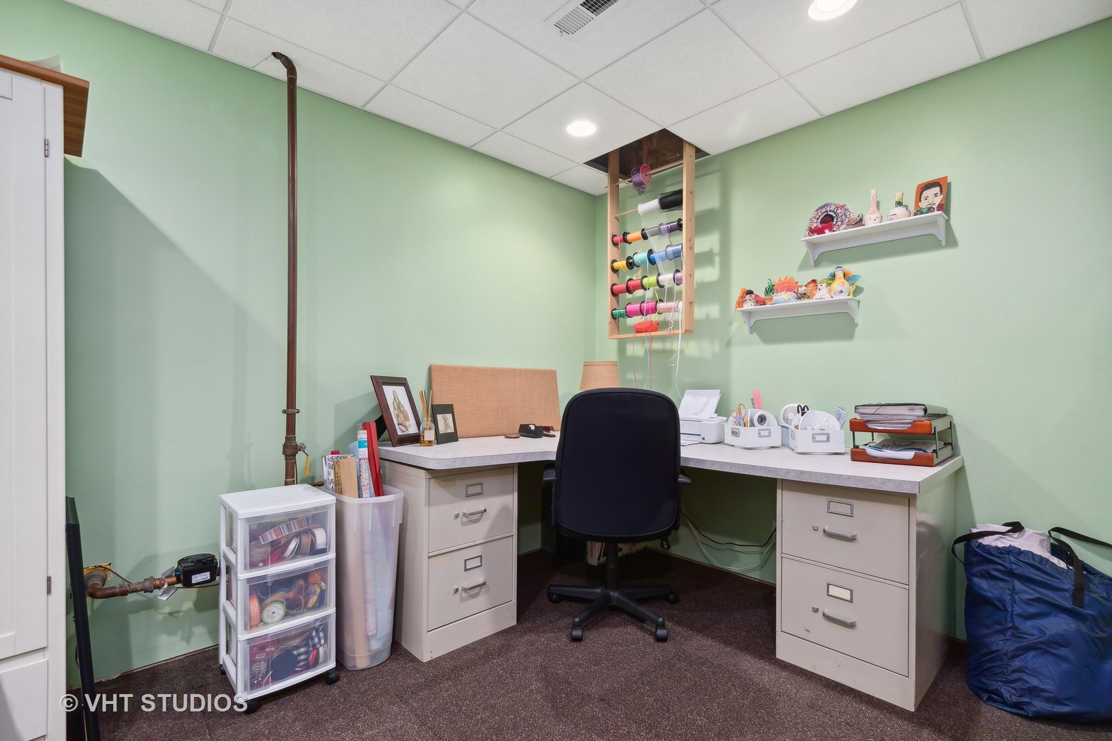 Home office and craft workspace with green walls, an L-shaped desk, and colorful thread spools.