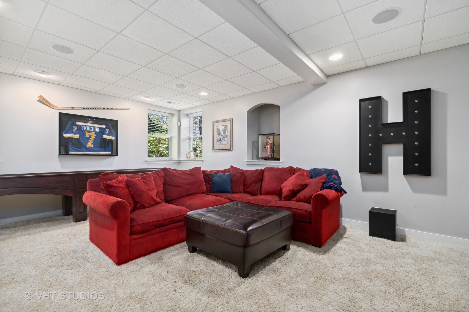 Recreation room with a red sectional, leather ottoman, and hockey memorabilia.