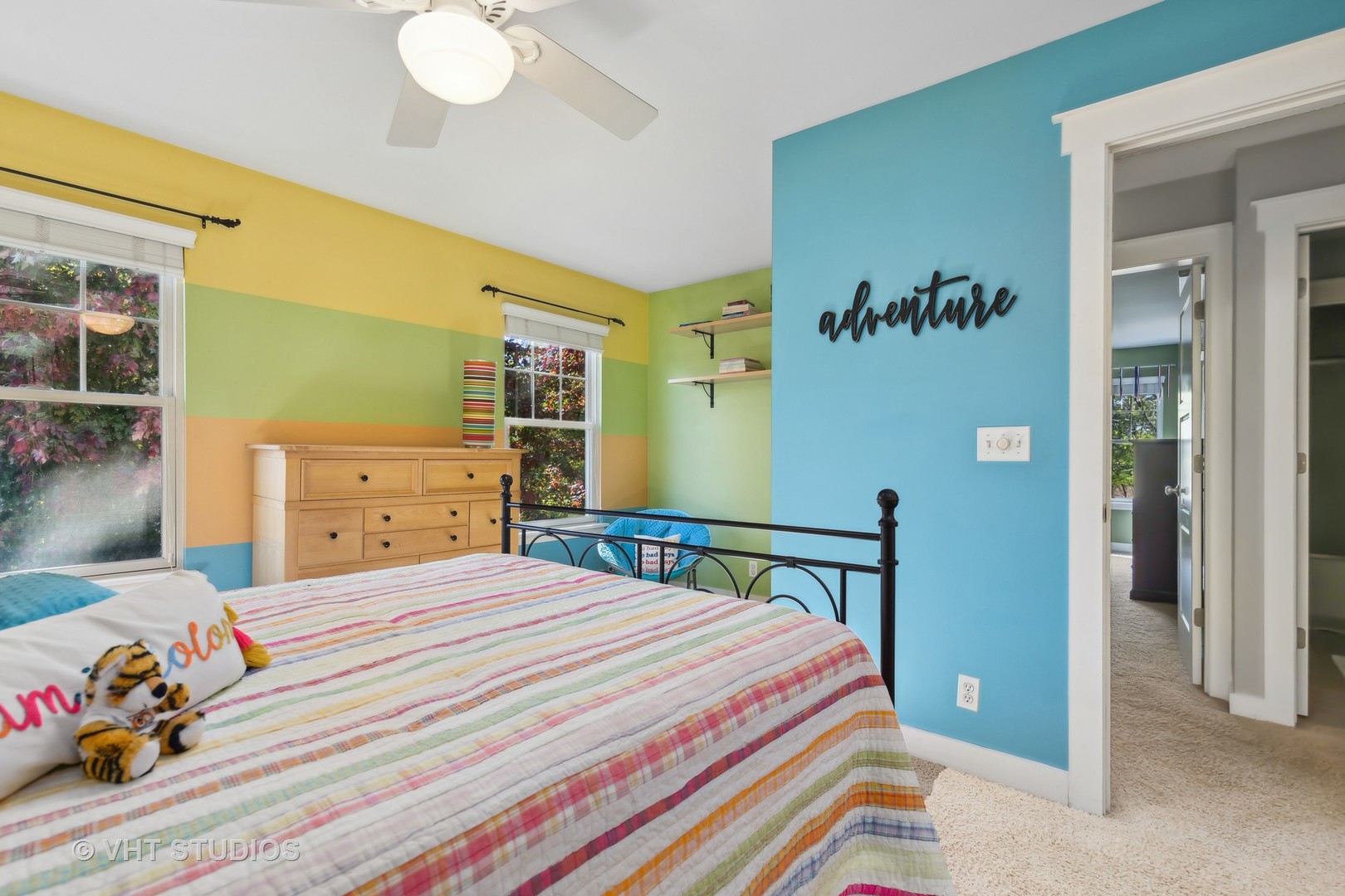 Bedroom with a striped quilt, black metal bed frame, and brightly colored walls.