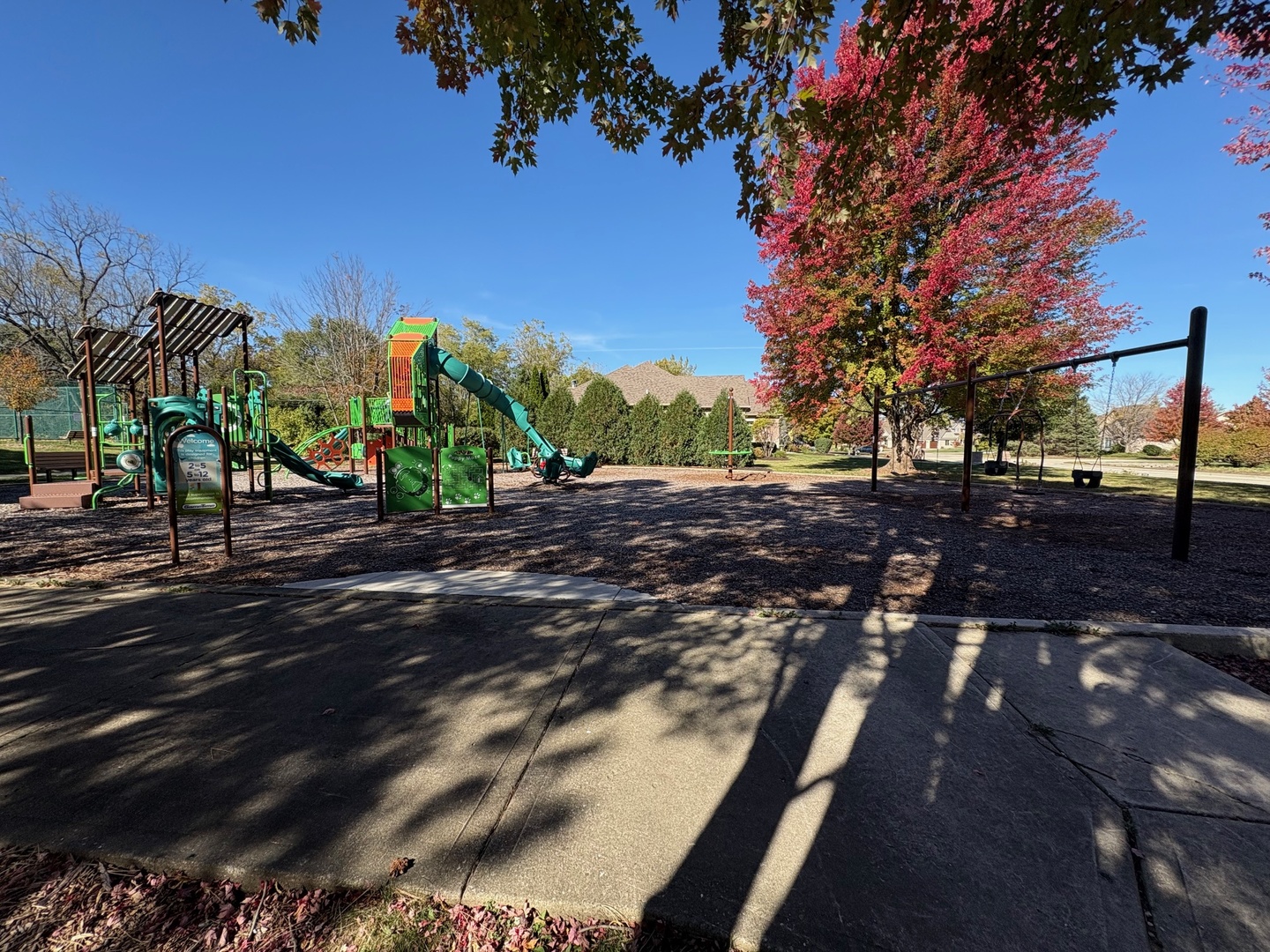 Neighborhood playground with colorful climbing equipment and swings beneath autumn trees.