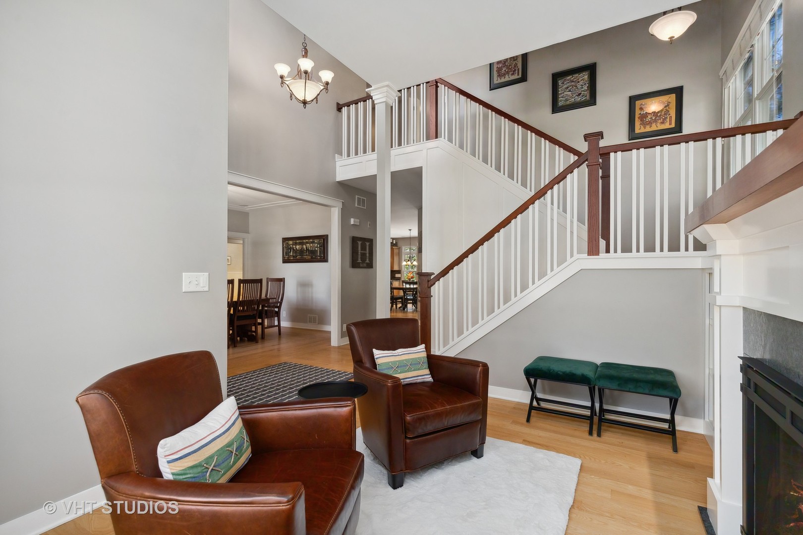 Living room with a sweeping white staircase, dark wood railings, and brown leather armchairs.