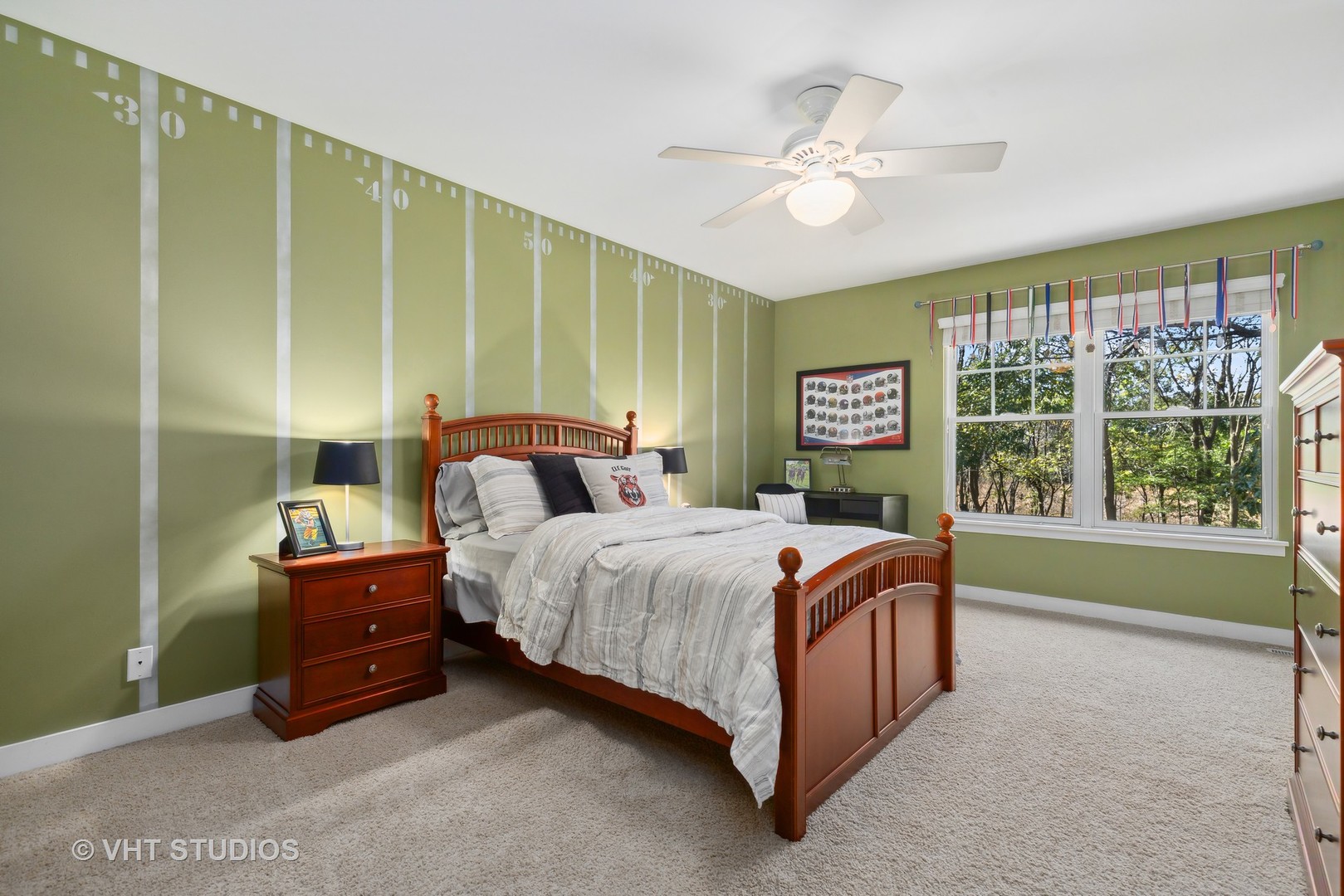 Bedroom with a wooden bed, green measuring-mark wall, and large window overlooking trees.