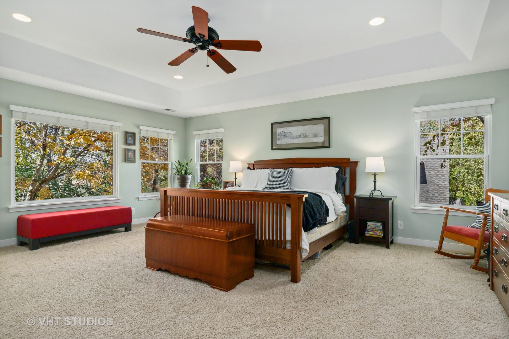Furnished bedroom with a dark wood four-poster bed, tray ceiling, and windows overlooking autumn foliage.
