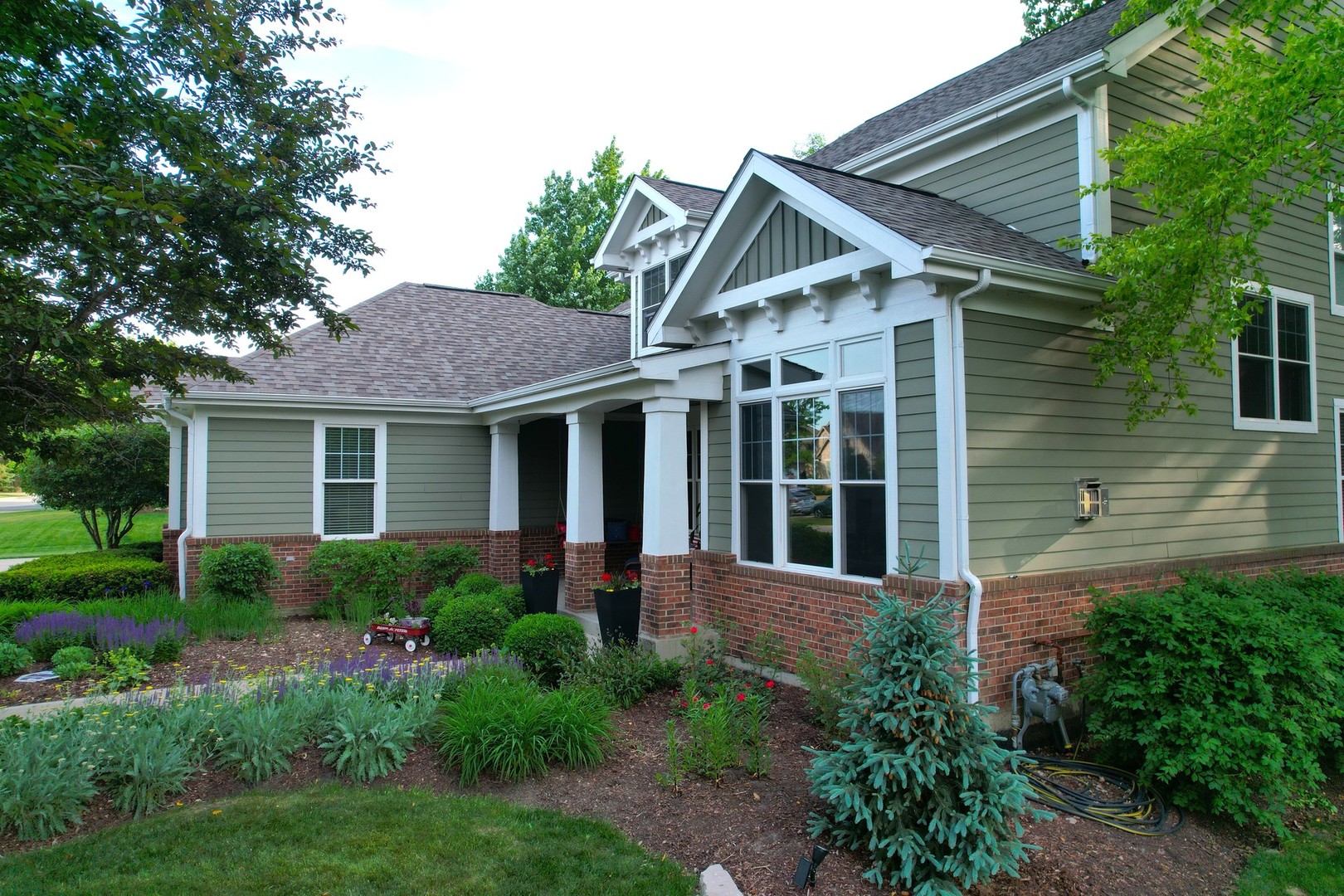 Sage-green two-story home with a covered entry, brick facade, and landscaped garden.
