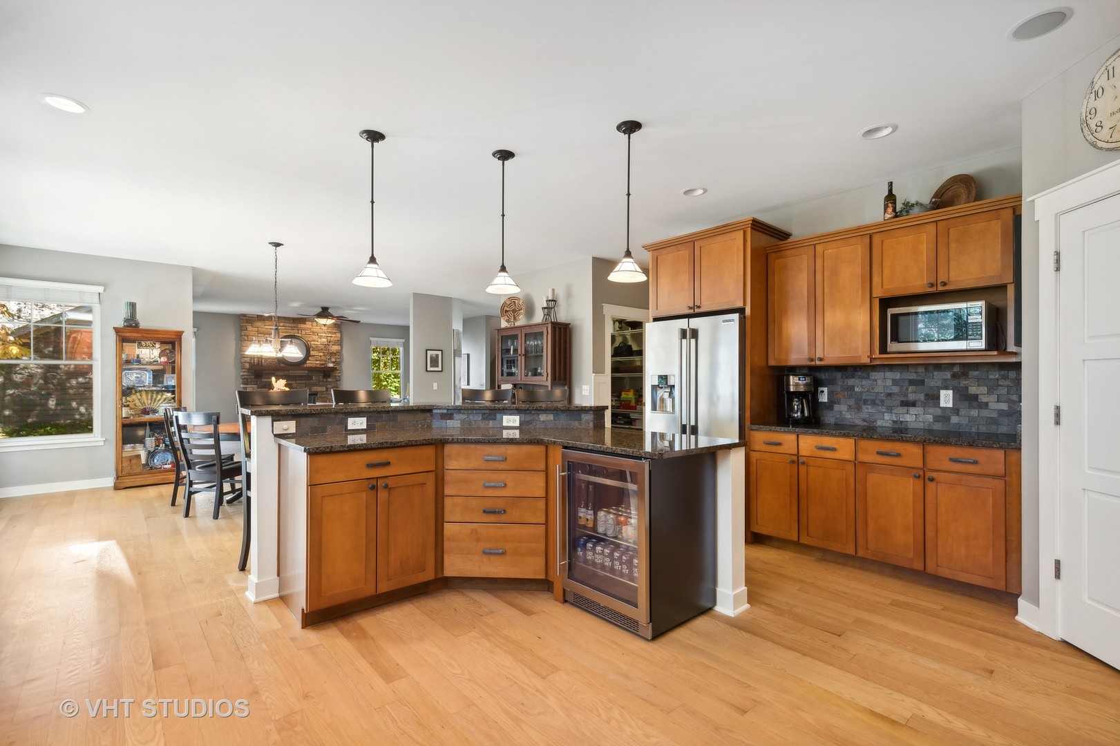 Open kitchen with warm wood cabinets, a large island, dark stone counters, and stainless steel appliances.