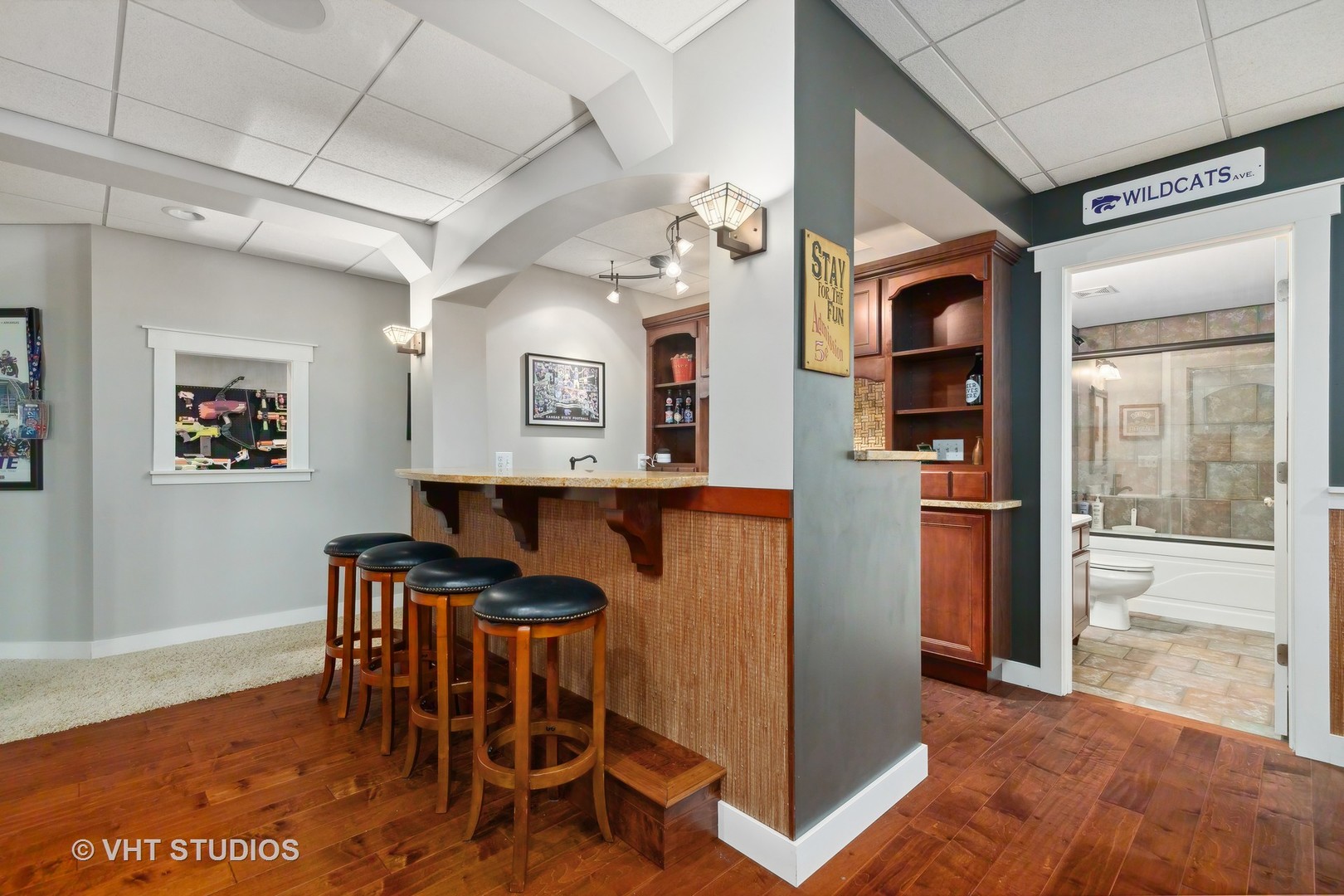 Finished basement bar with four stools, wood cabinetry, and a bathroom doorway.
