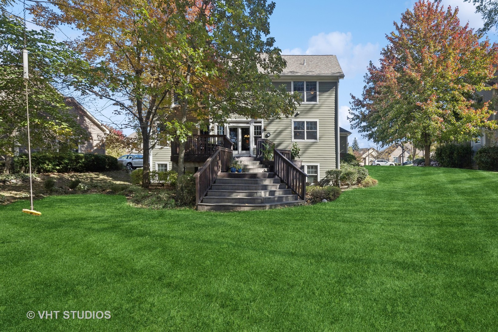 Rear of a two-story green house with a raised deck, broad stairs, and spacious lawn.