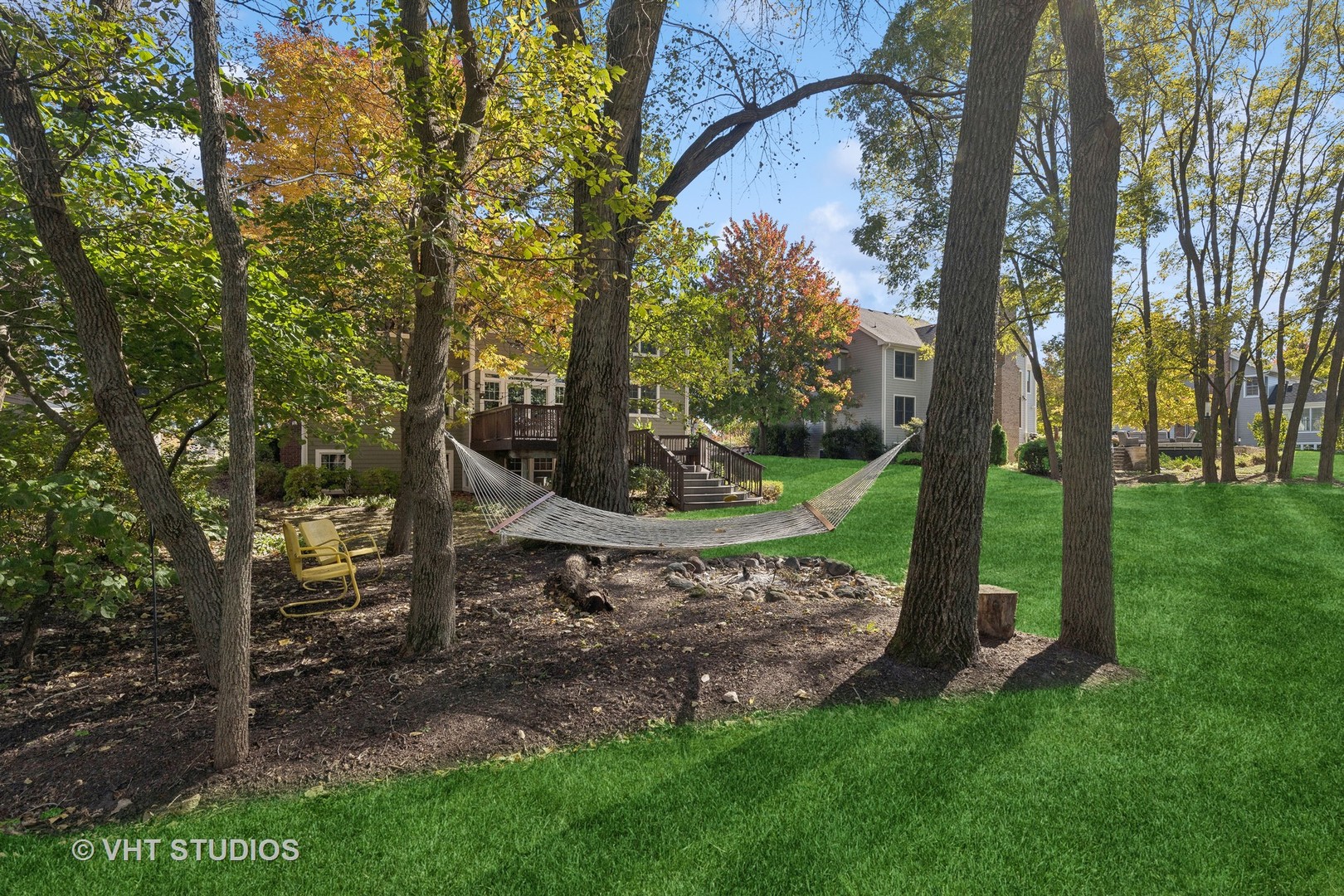 Wooded backyard with a hammock, raised deck, and green lawn behind the home.