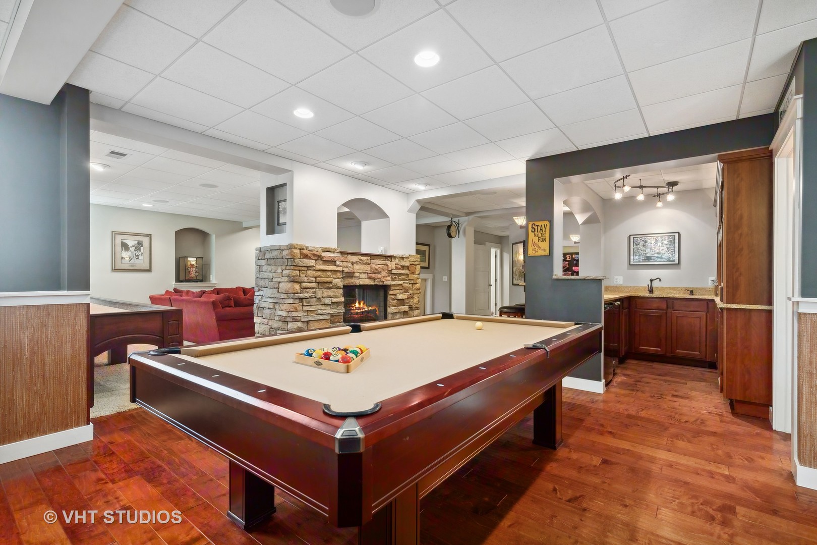 Recreation room with a billiards table, stone fireplace, red seating, and a wood-cabinet bar.