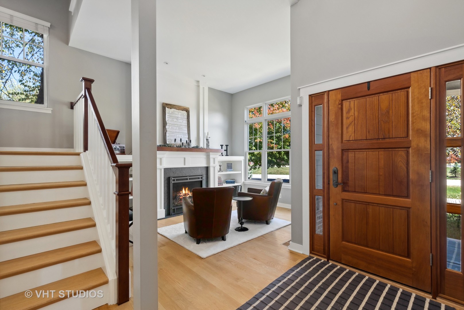 Entry foyer with a paneled wood front door, staircase, and fireplace seating area.