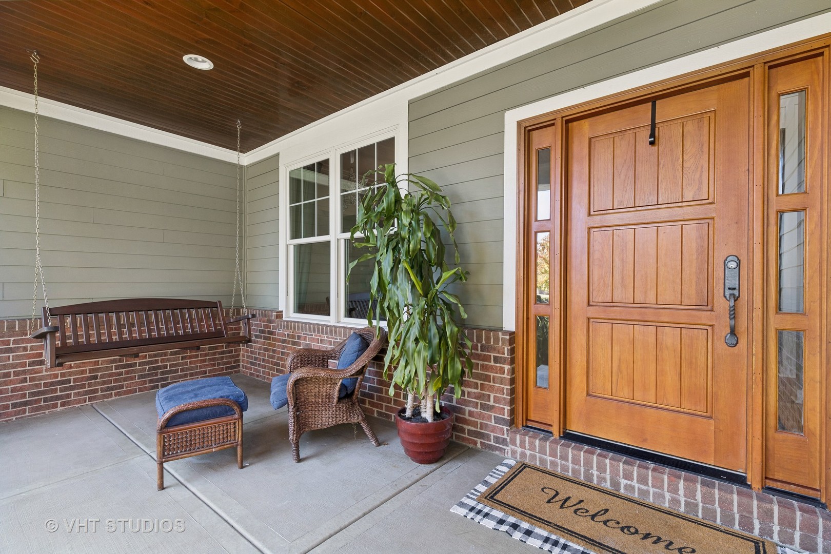 Covered front porch with a wooden entry door, hanging swing, and wicker seating.