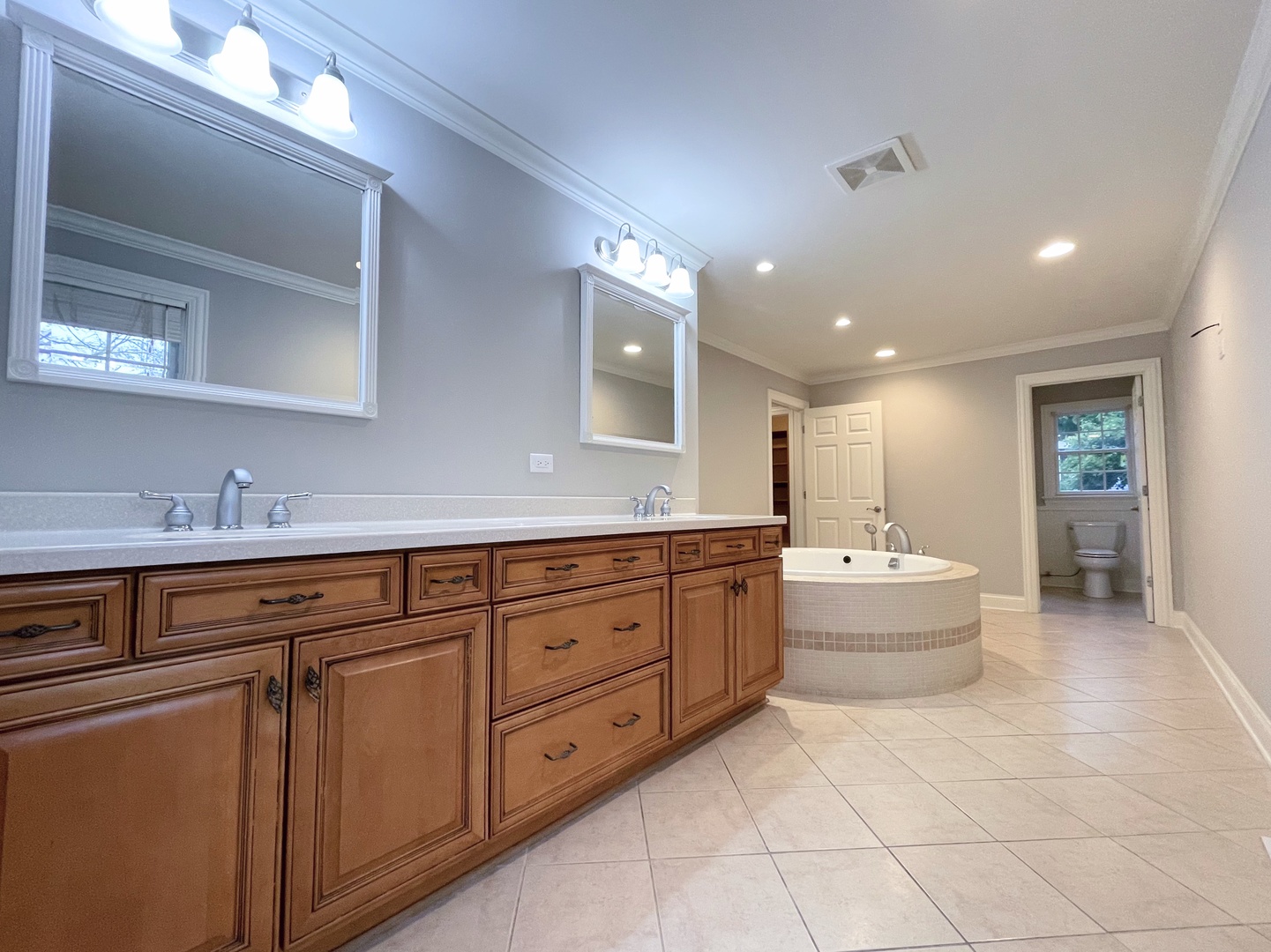 Bathroom with a long wood vanity, tiled soaking tub, and separate toilet room.