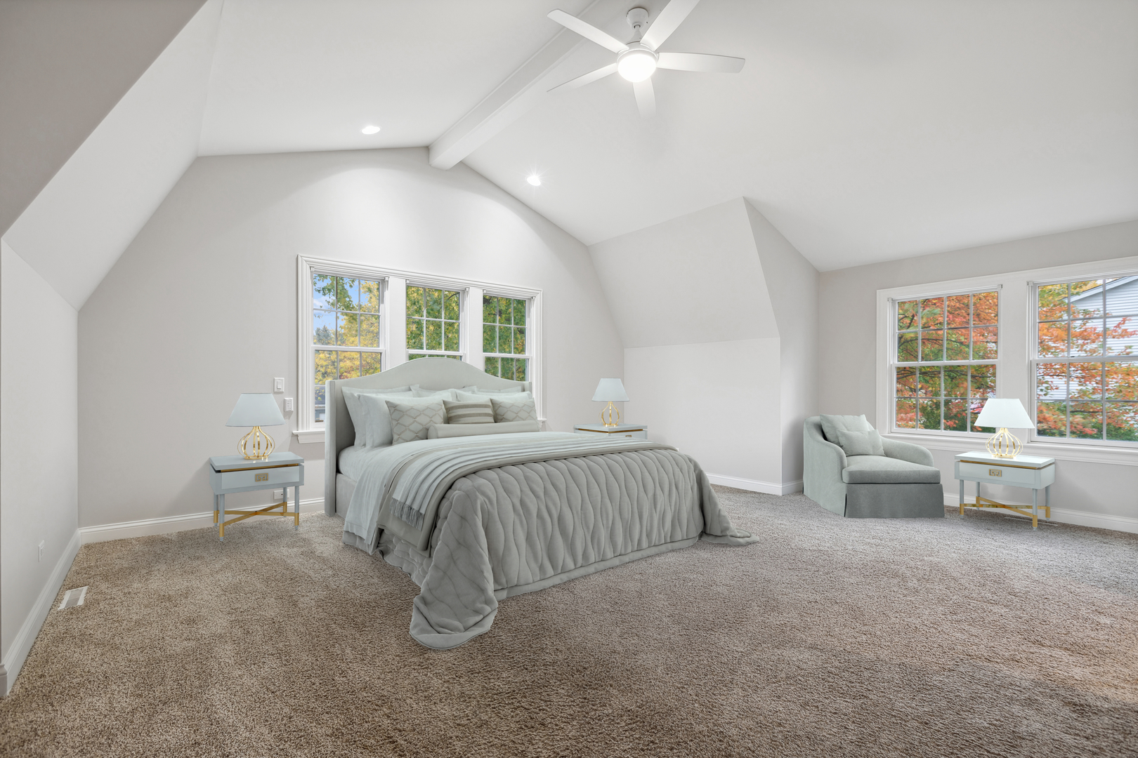 Staged bedroom with a large bed, vaulted ceiling, and windows overlooking autumn foliage.