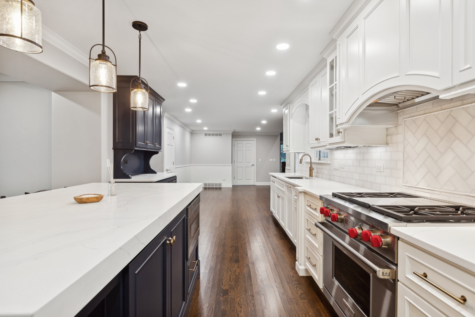 Renovated kitchen with a large stone island, white cabinetry, dark accents, and a professional gas range.