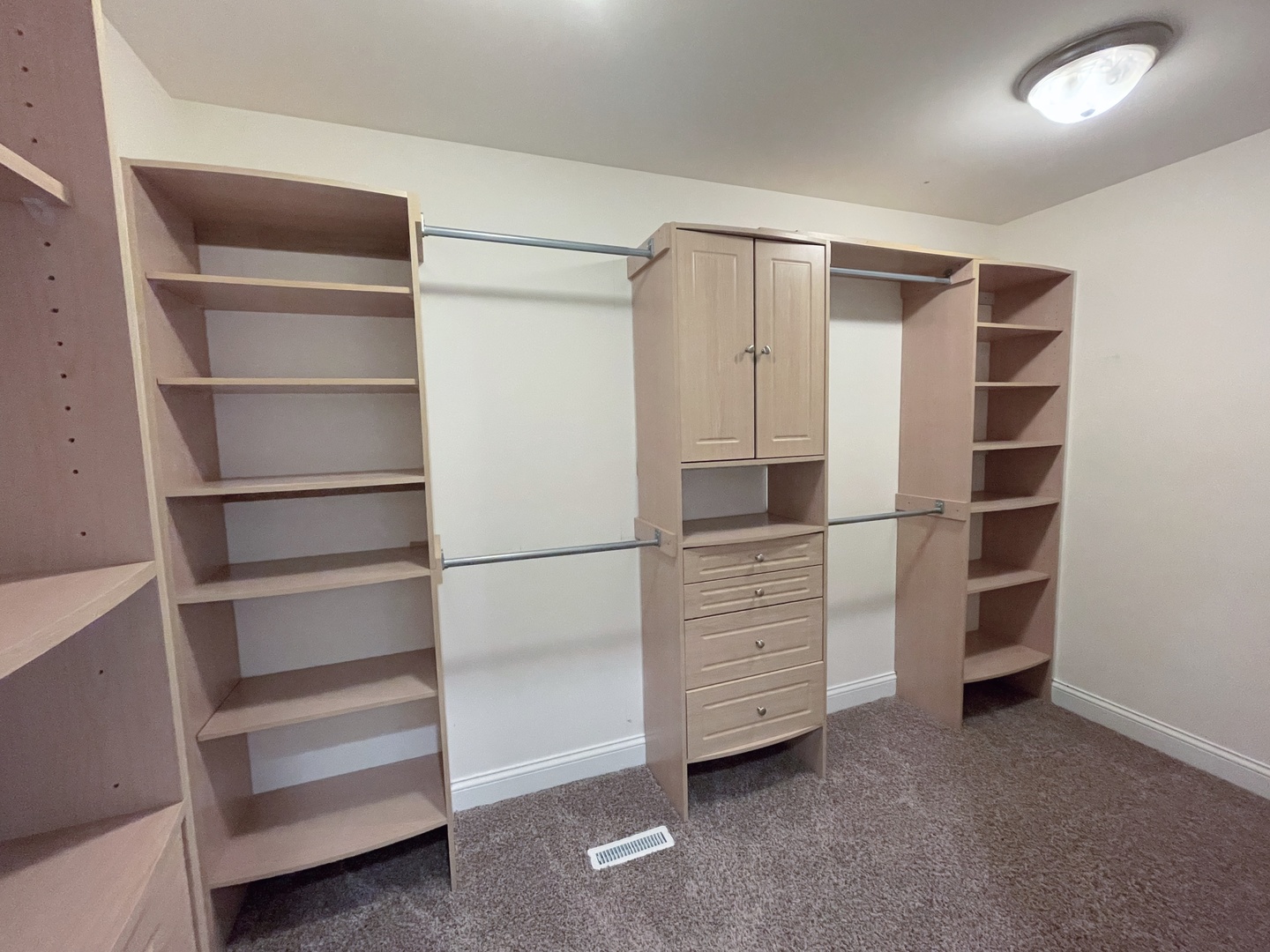 Walk-in closet with built-in shelving, hanging rods, and a central cabinet with drawers.