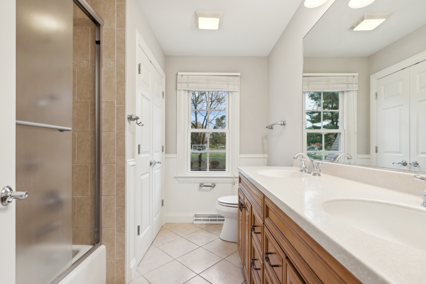 Bathroom with tiled shower, long wood vanity, double sinks, and two windows.