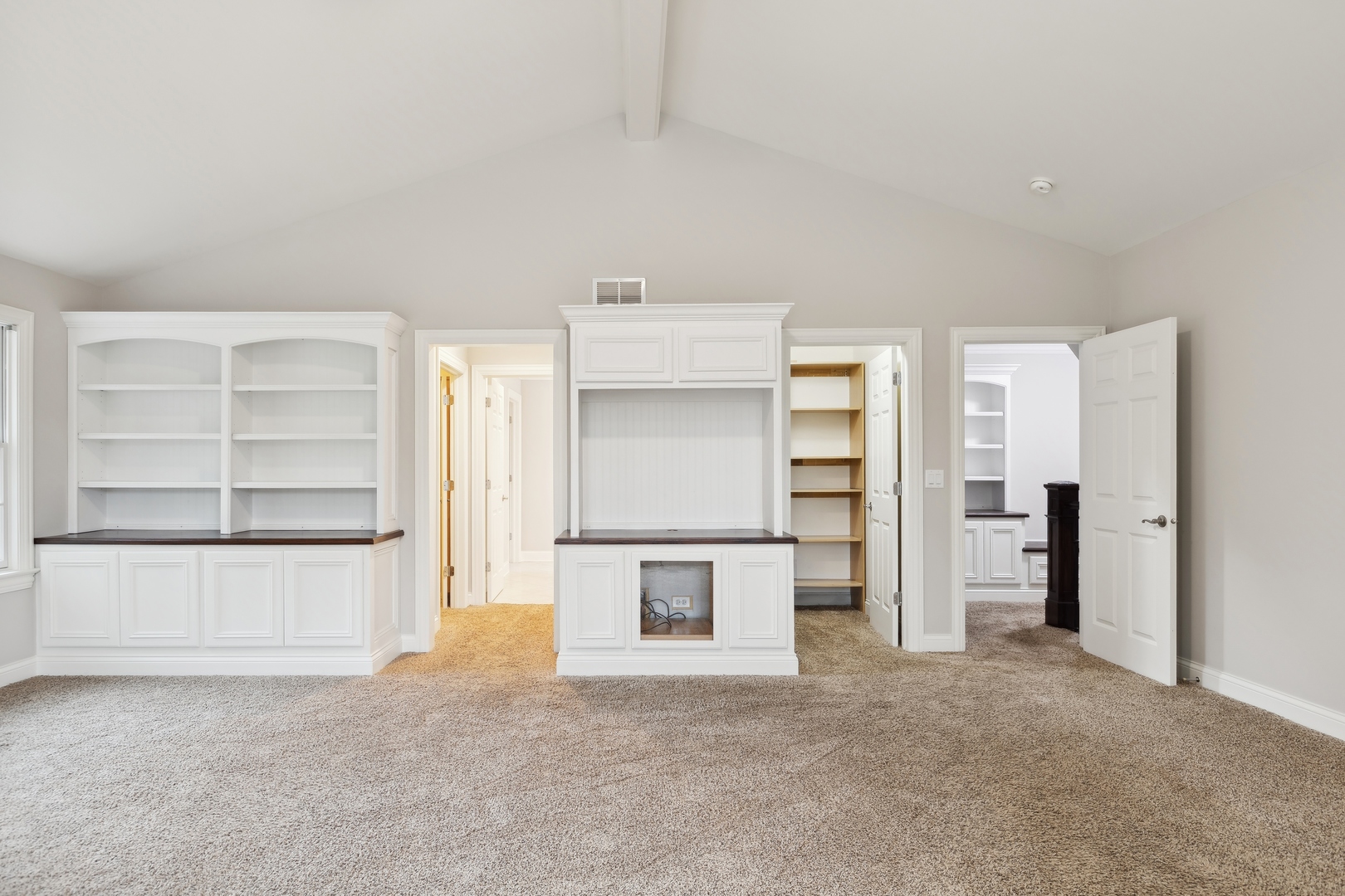 Carpeted room with vaulted ceiling and extensive white built-in cabinetry.