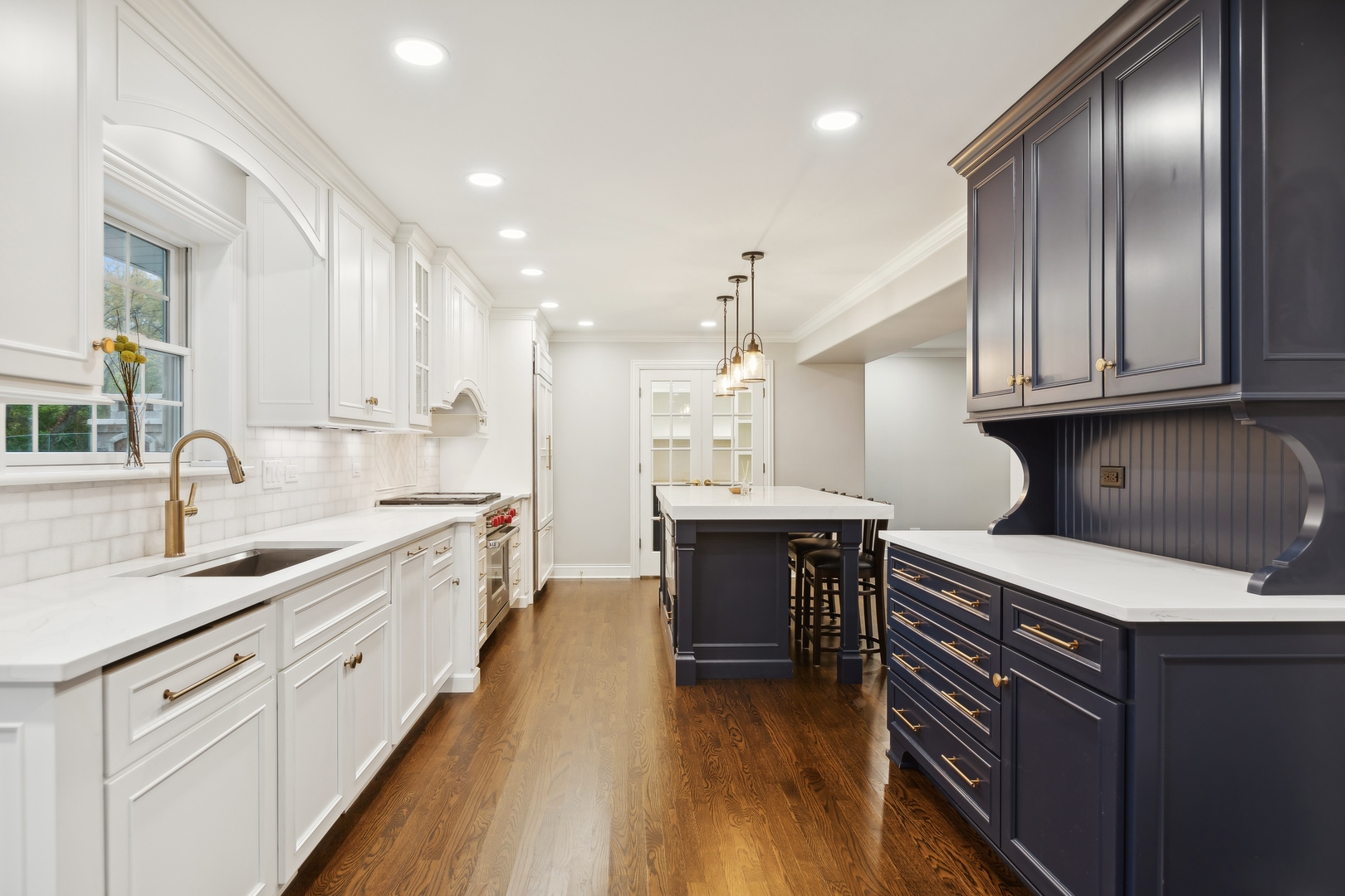 Kitchen with navy island and cabinetry, white cabinets, brass fixtures, and hardwood floors.