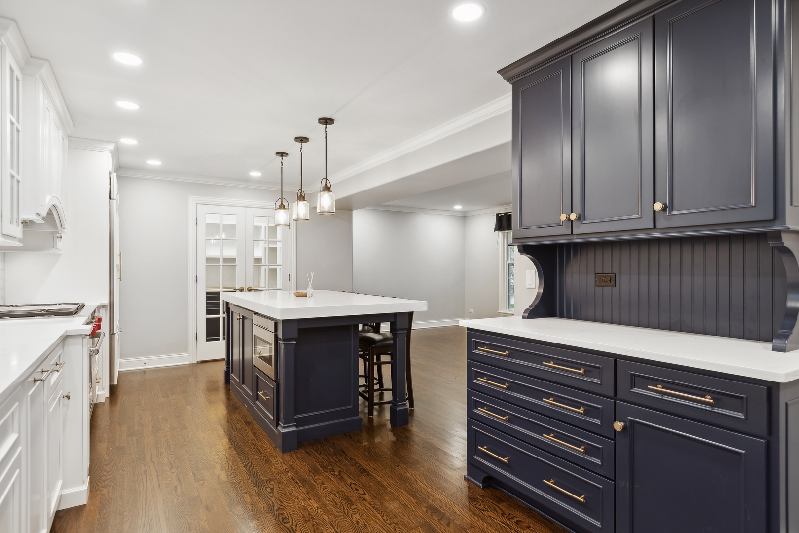 Kitchen with a navy island and cabinetry, white counters, brass hardware, and hardwood floors.