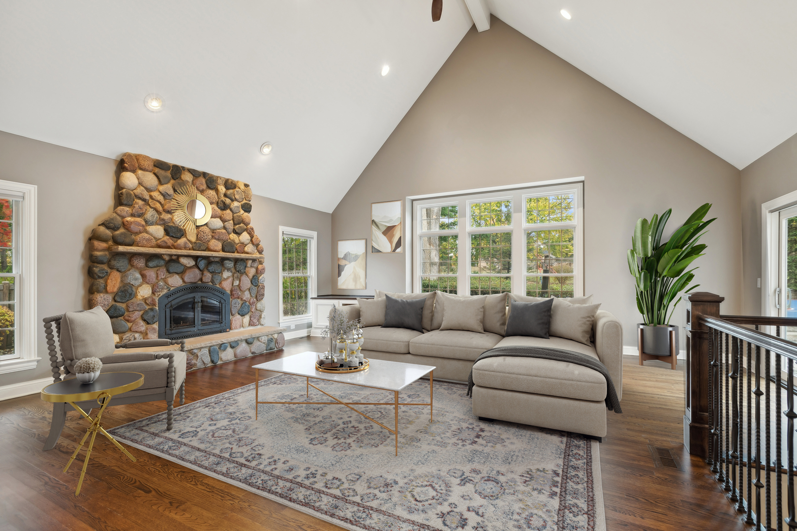 Living room with vaulted ceiling, stone fireplace, beige sectional, and tall windows.