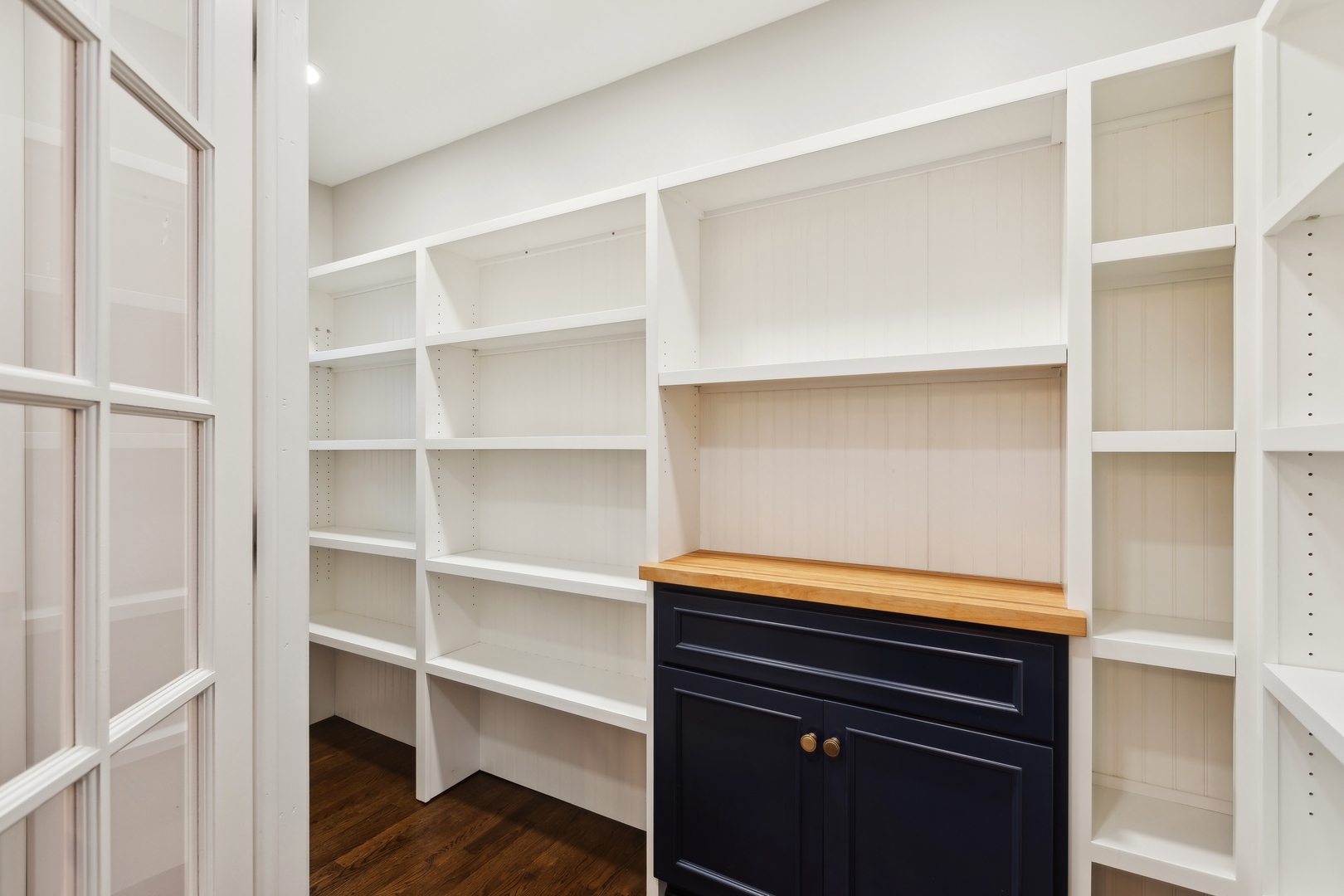 Built-in pantry with white open shelves, navy cabinet, and butcher-block countertop.