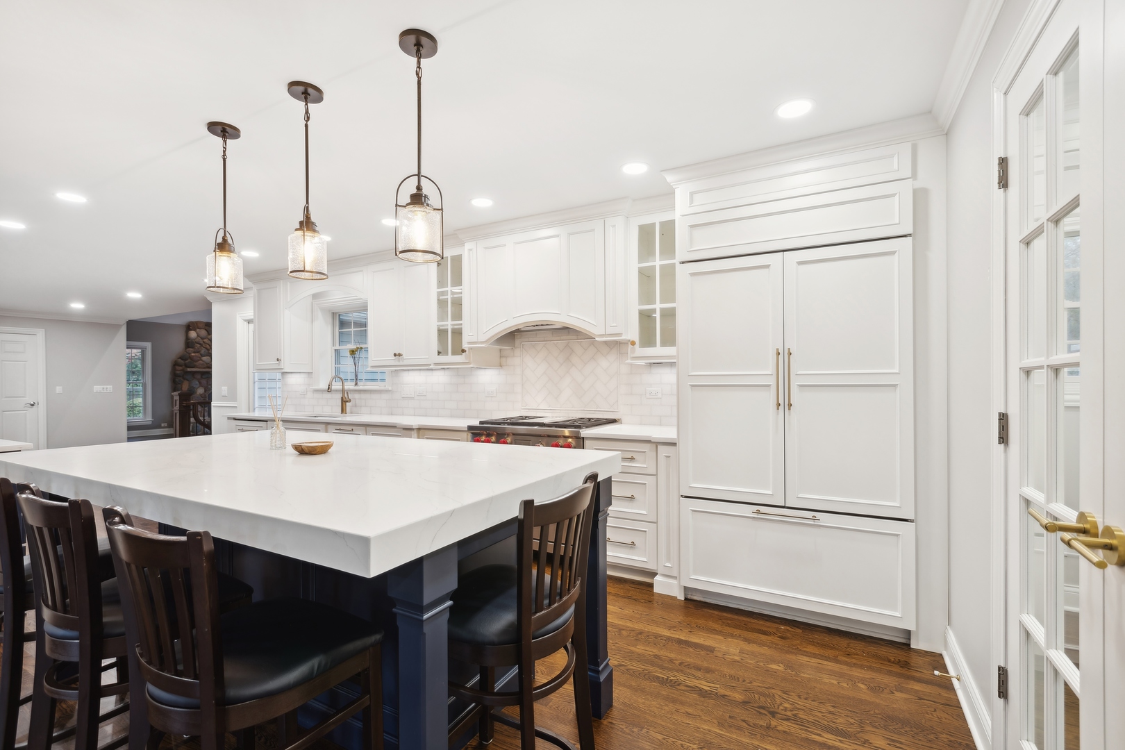 Bright white kitchen with a large stone island, dark stools, brass pendant lights, and warm hardwood floors.