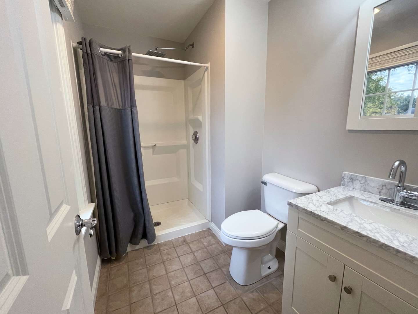 Bathroom with a curtained walk-in shower, white toilet, and marble-look vanity countertop.