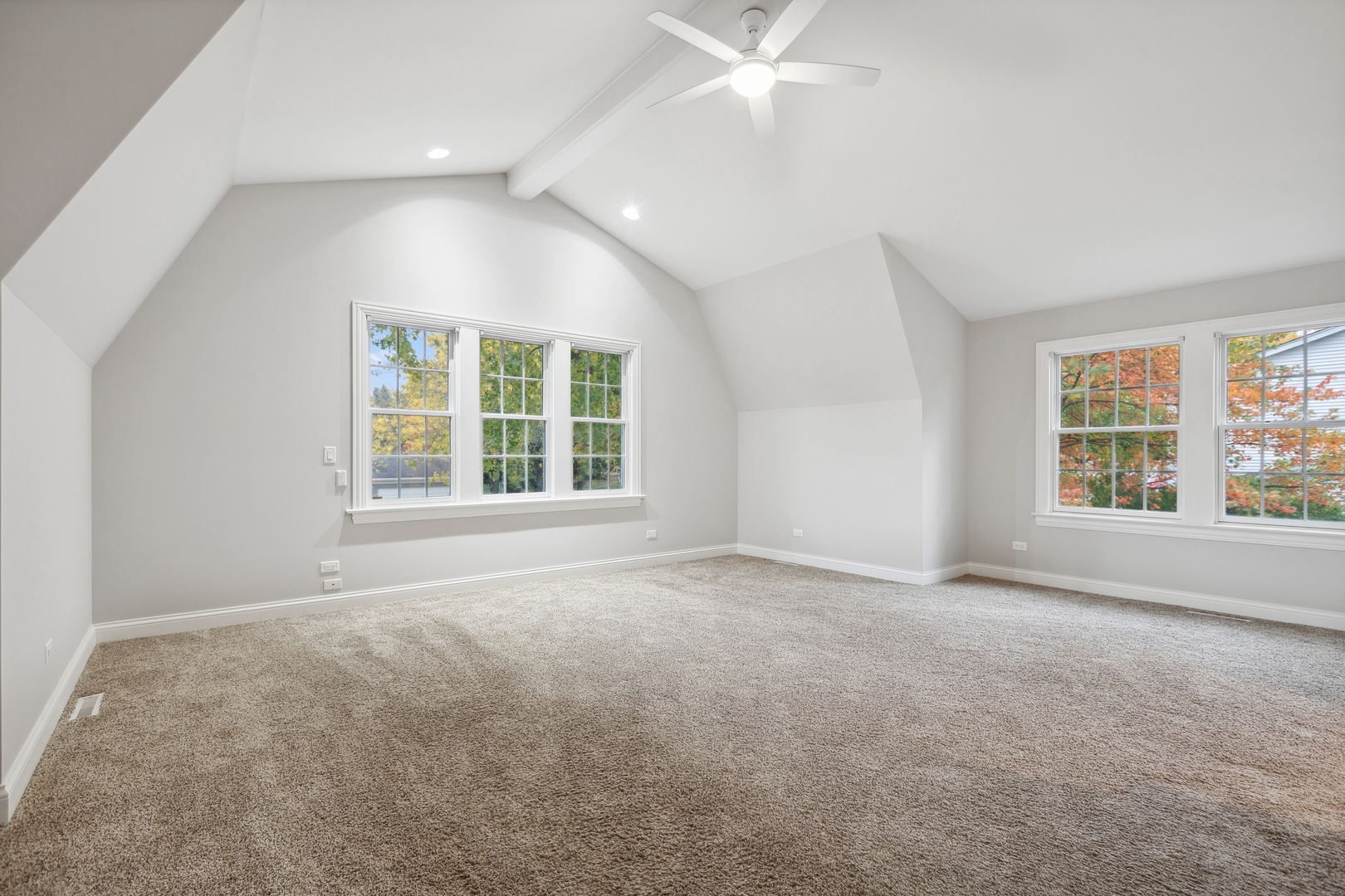 Empty carpeted upper-level room with a vaulted ceiling, ceiling fan, and large windows.