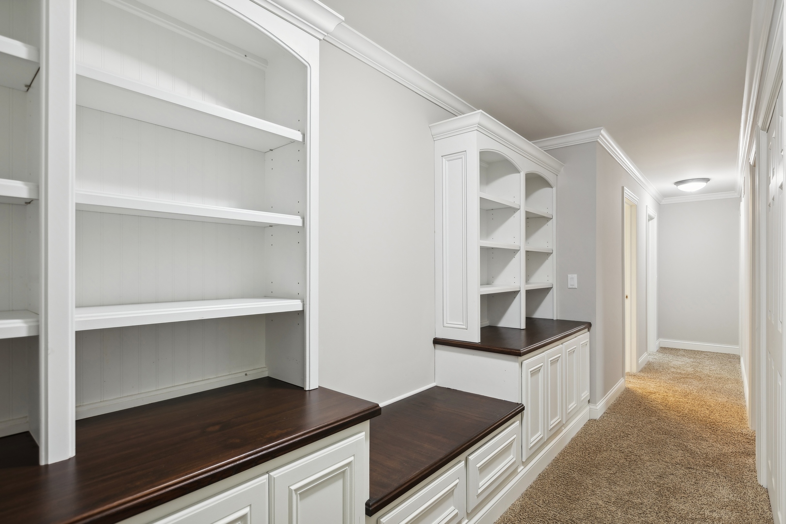 Hallway with built-in white shelving and dark wood countertops beside a carpeted corridor.