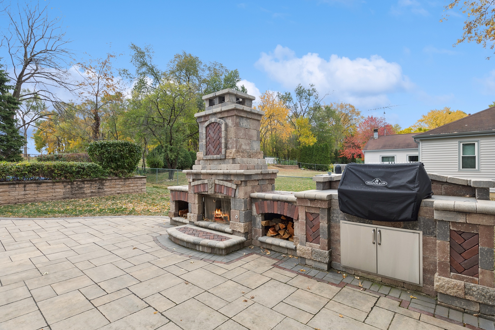 Paved patio with a large stone fireplace, built-in wood storage, and covered grill.